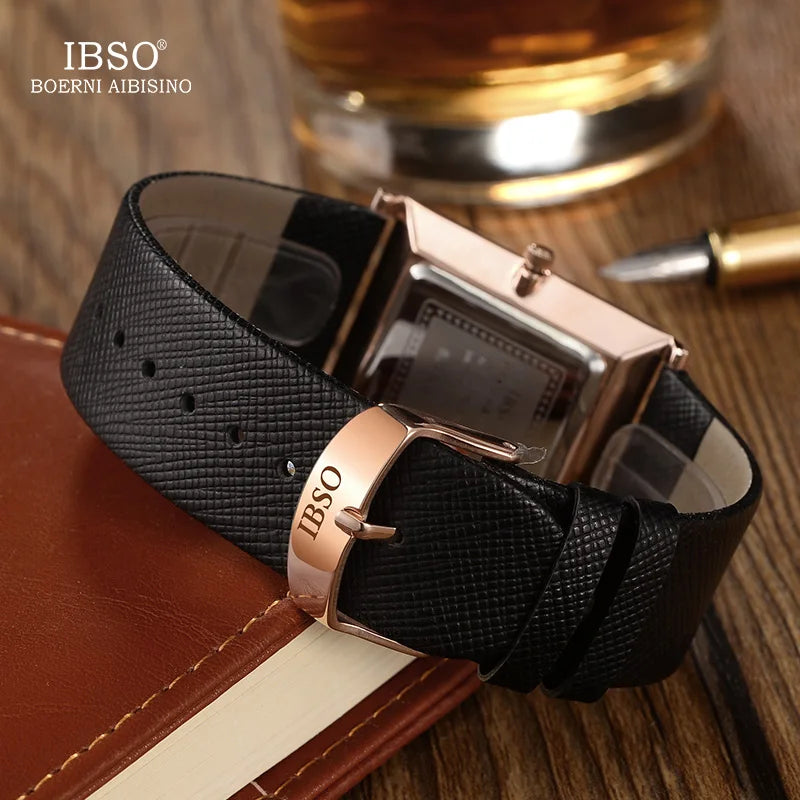 Close-up view of the back of the IBSO watch strap showing the black genuine leather texture, rose gold buckle clasp, and case back resting on a notebook