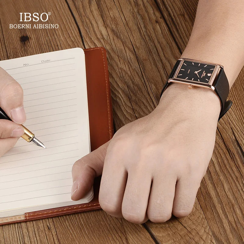 A man wearing the IBSO rose gold and black dial rectangular watch on his wrist while writing in a leather notebook on a wooden desk