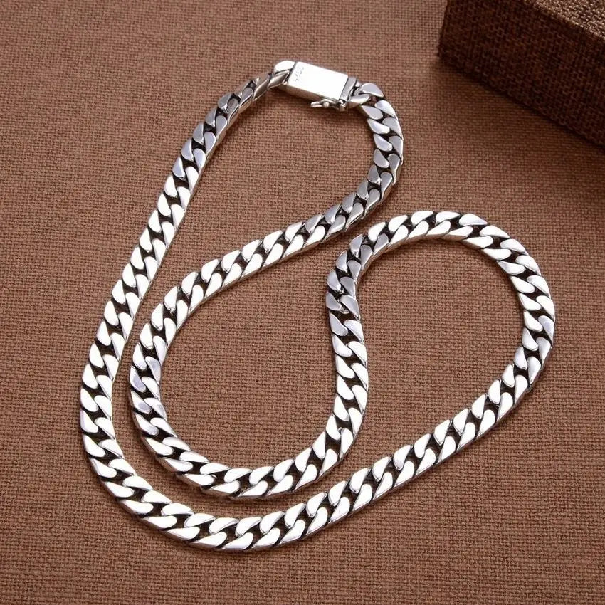 Men's thick silver Cuban chain resting on a warm brown textured fabric background.