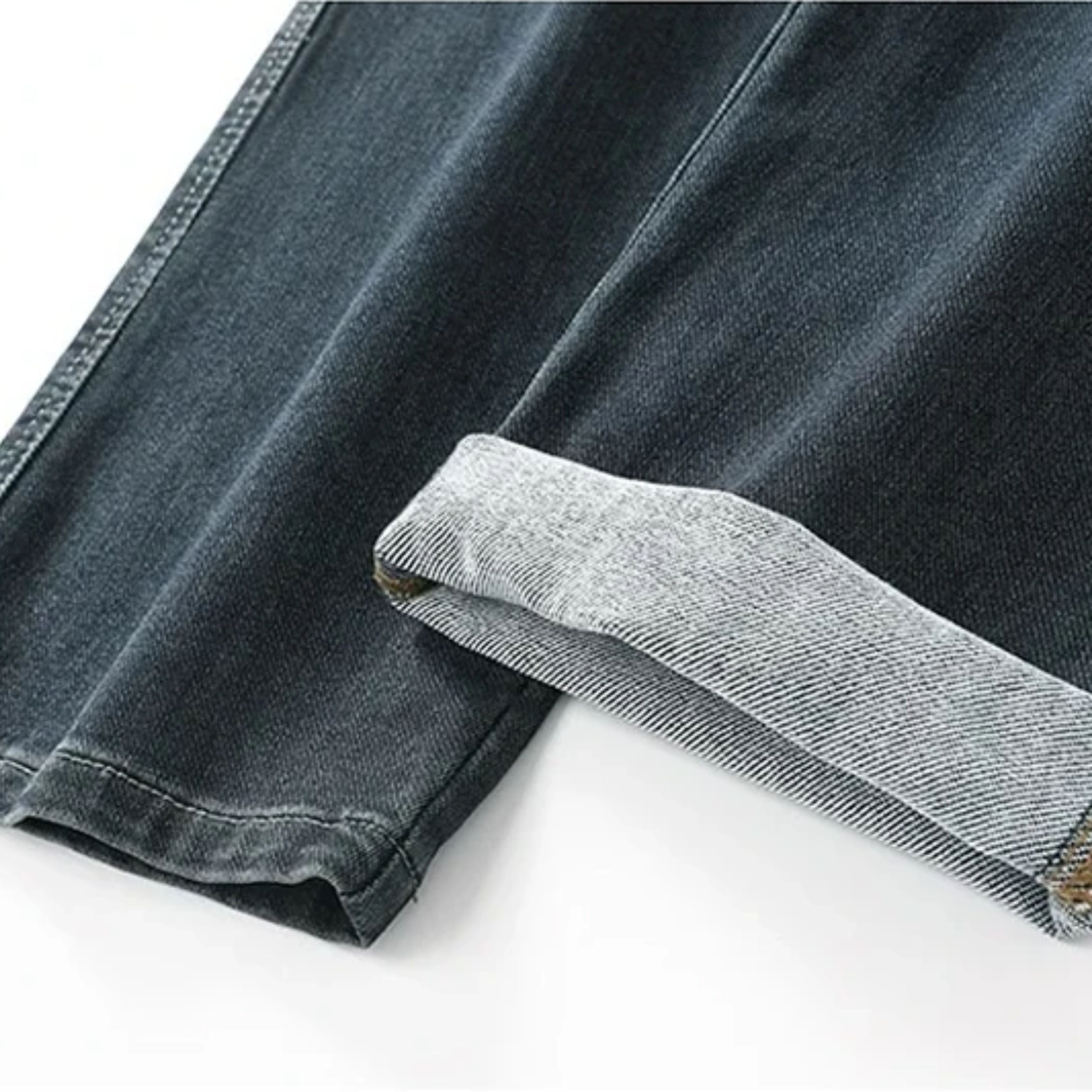 Close-up macro shot of the dark denim pants hem with a turned-up ankle cuff, demonstrating the high-quality interior chain-stitch lines