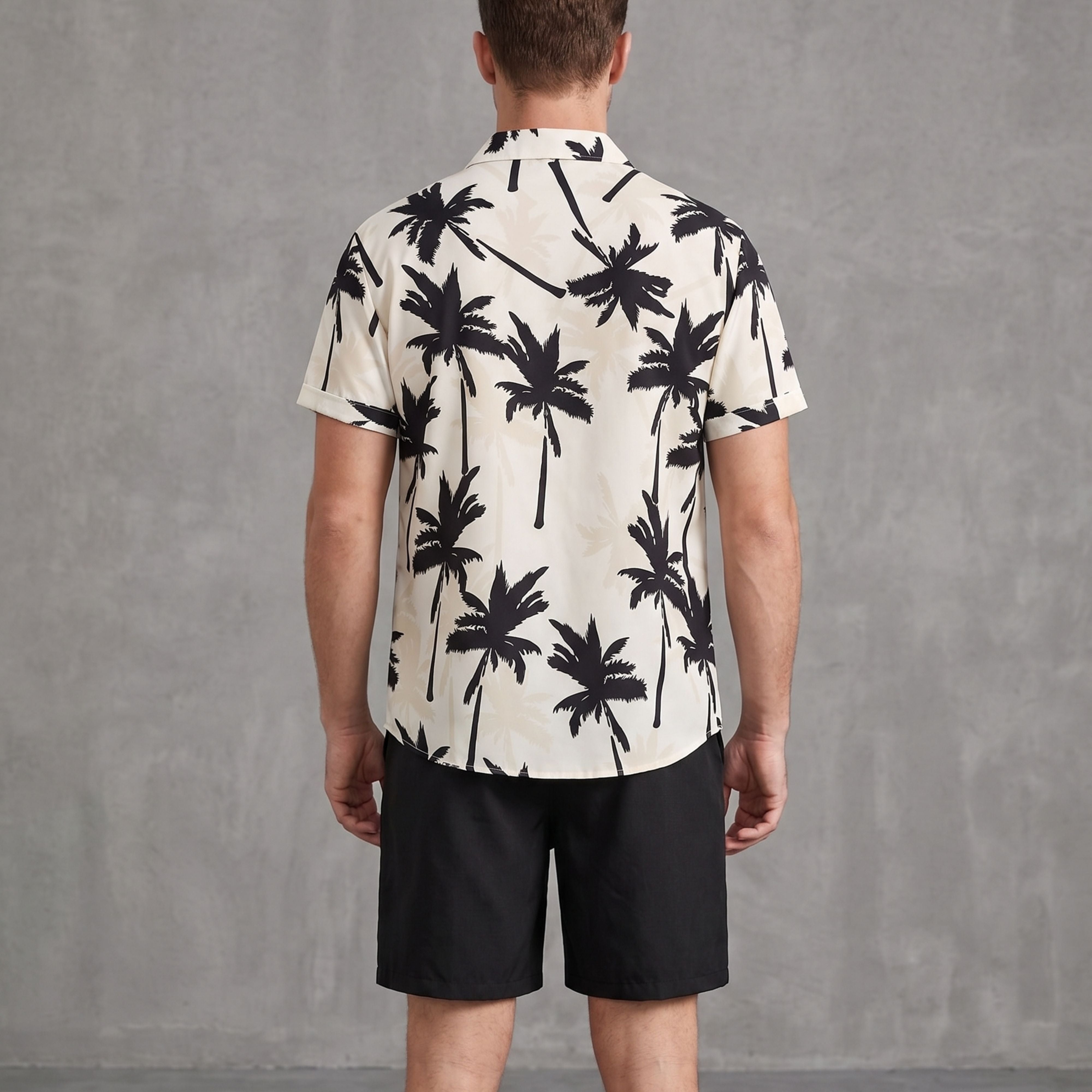 Rear view of a male model showcasing the back layout of the single-breasted white and black palm tree printed shirt paired with casual black shorts