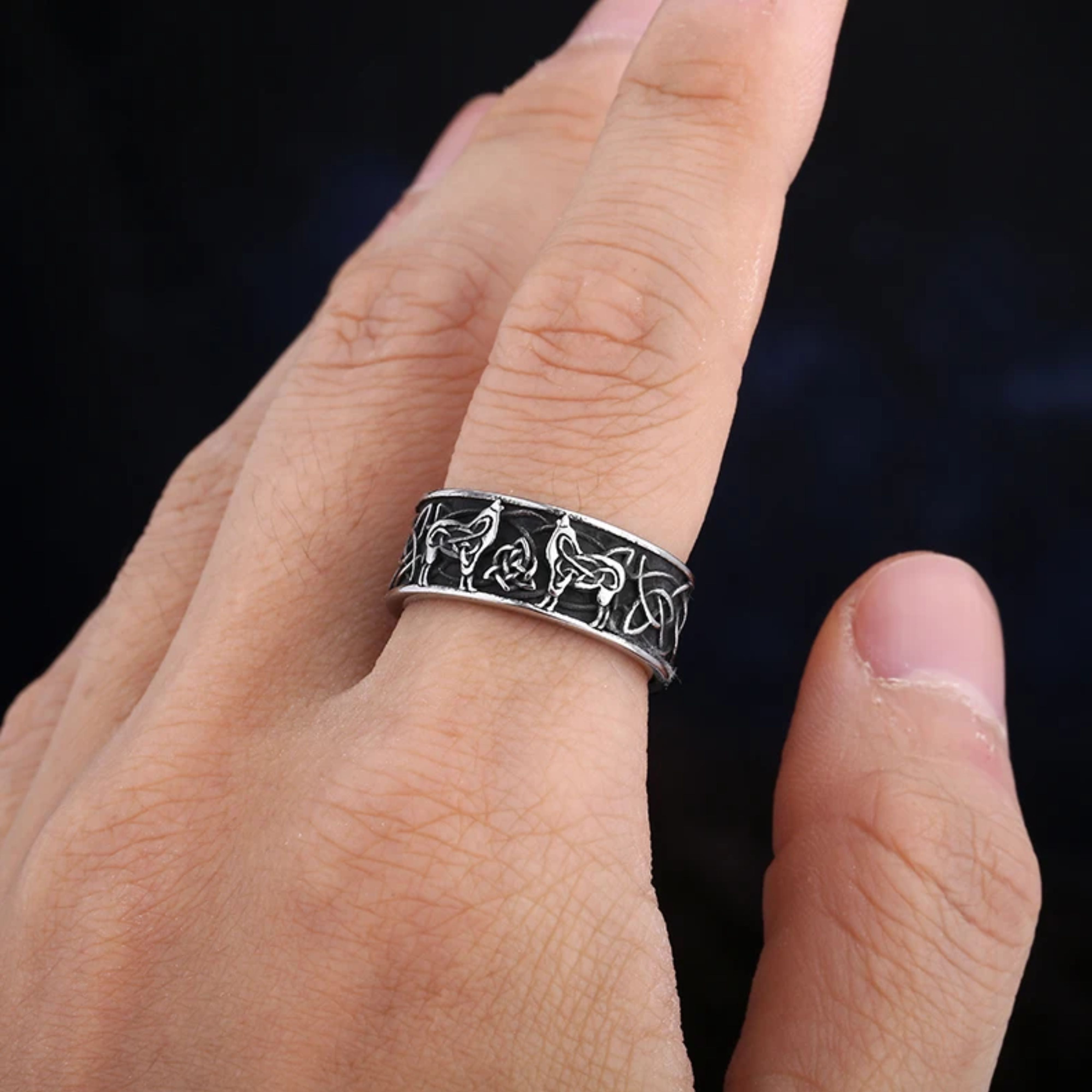 Men's silver Viking band ring with wolf and Celtic knot design being worn on a finger against a dark background.