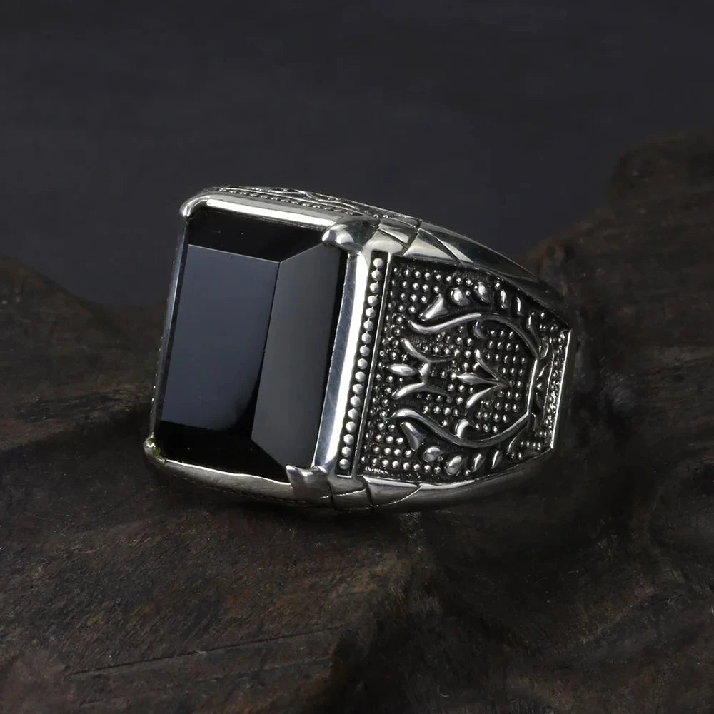 Oxidized silver men's ring with a large black rectangular stone resting on dark grey slate.