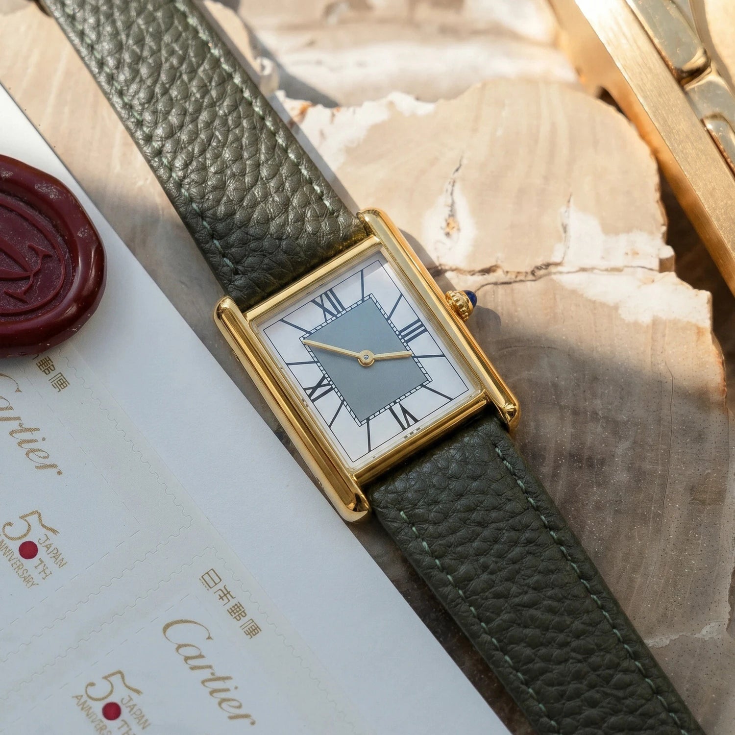 Retro rectangular gold watch with an olive green leather strap beautifully displayed on top of vintage letters next to a classic red wax seal.