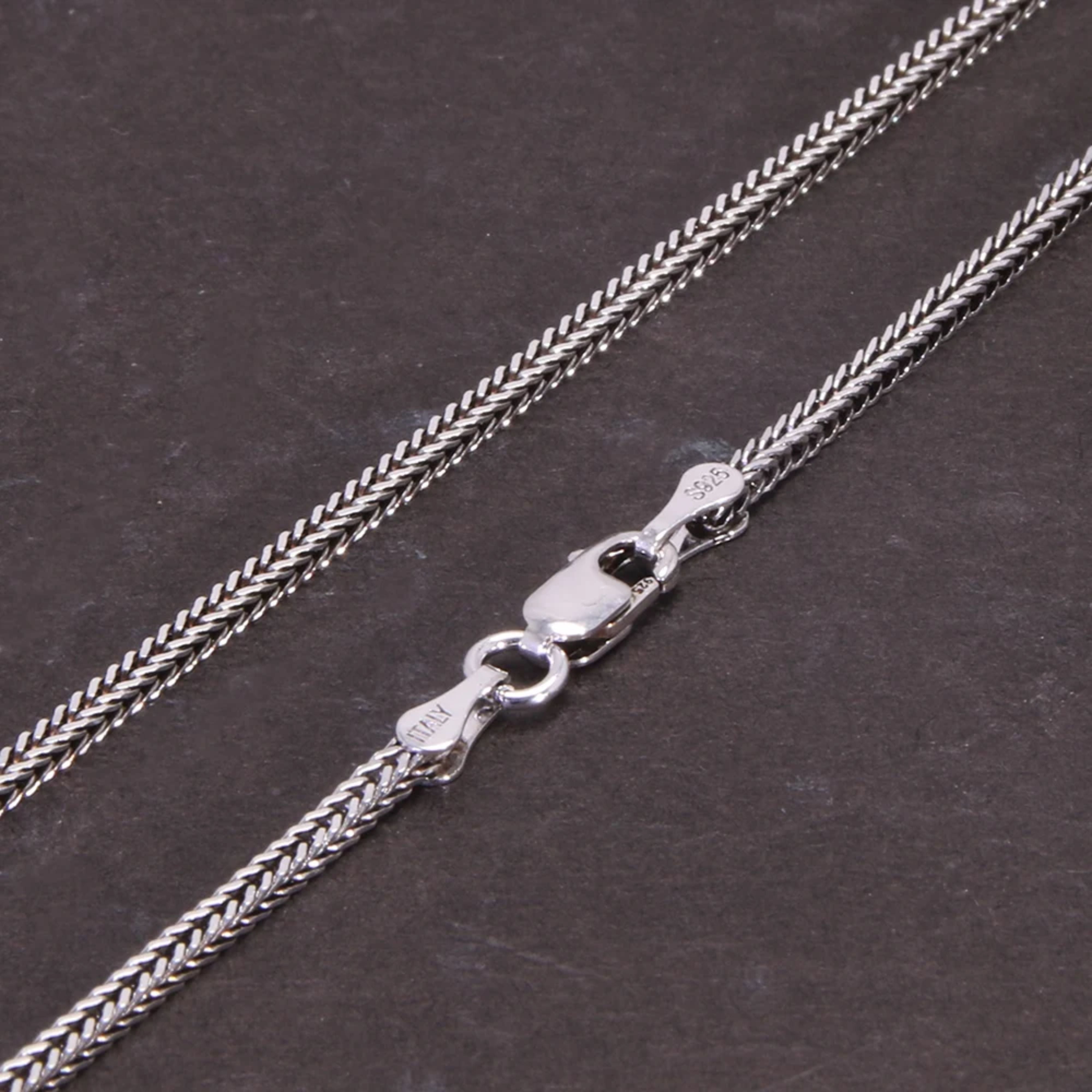Detailed macro view of the secure lobster claw clasp on a vintage silver woven chain against a dark background.