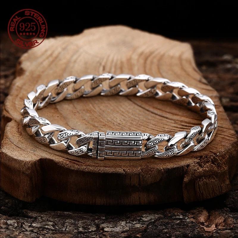 Silver Cuban chain bracelet with an engraved box clasp resting flat on a rustic wooden log slice.
