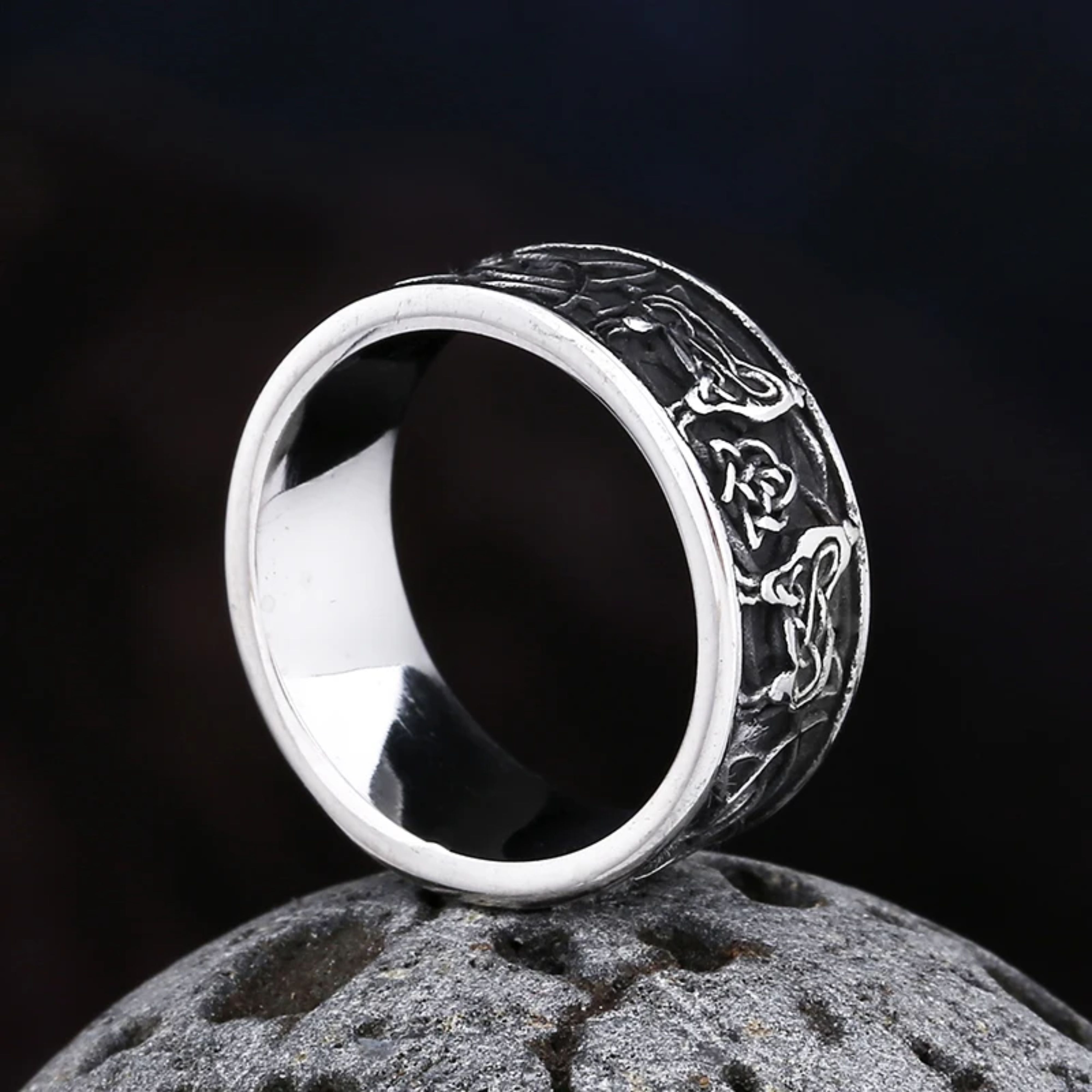Silver Celtic wolf band standing upright on a dark textured stone, highlighting the polished inner band and the oxidized outer design.