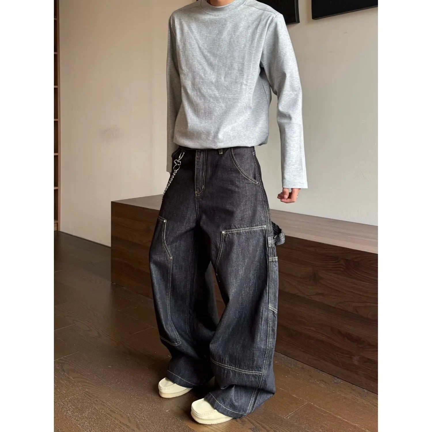 Model styling a minimalist long sleeve shirt with faded dark gray wide-leg denim pants in a modern architectural indoor space