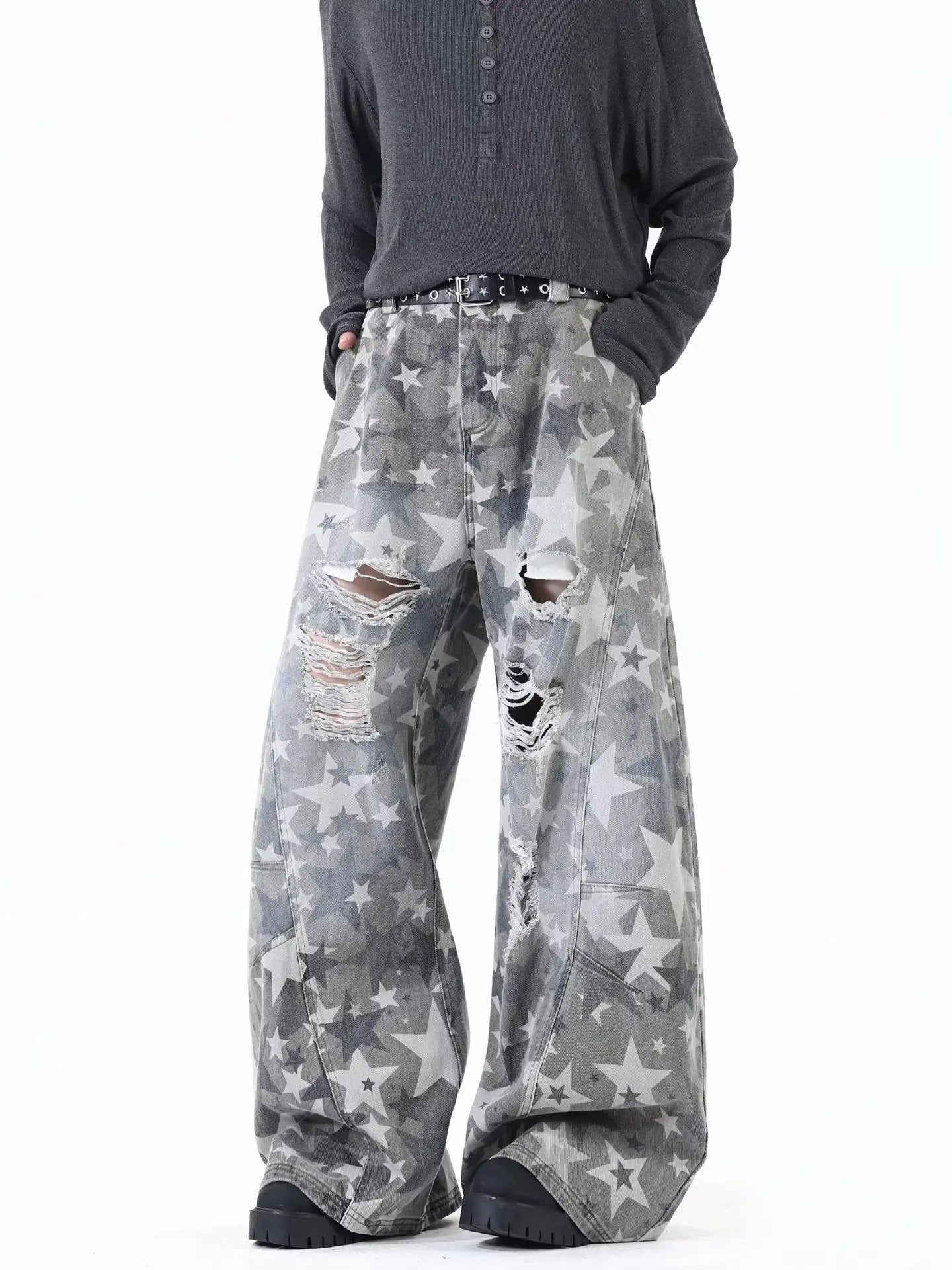 Model wearing gray high-streetwear wide-leg trousers covered in an all-over distressed star pattern print.