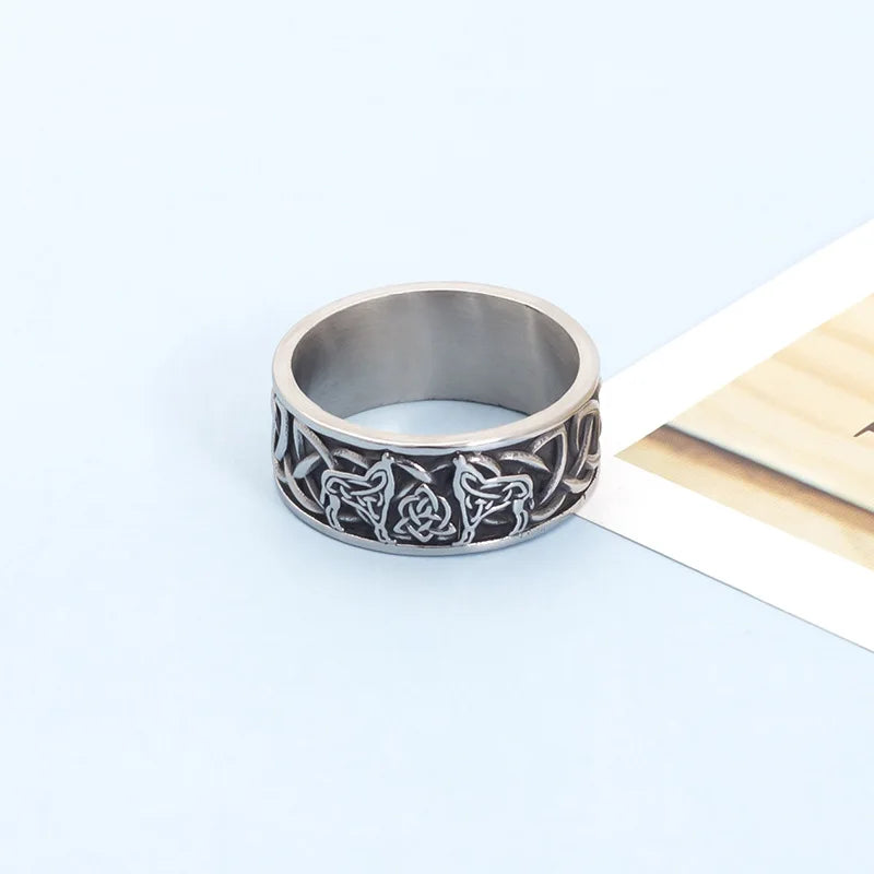 Vintage style silver Celtic knotwork and wolf ring resting flat on a light blue surface next to a white card.