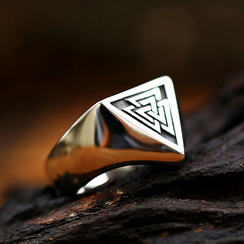 Vintage style silver Valknut signet ring resting on a dark blue textured stone background.