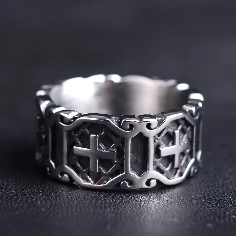 Wide silver band ring with raised cross motifs lying flat on a dark surface, showcasing its uniform thickness.