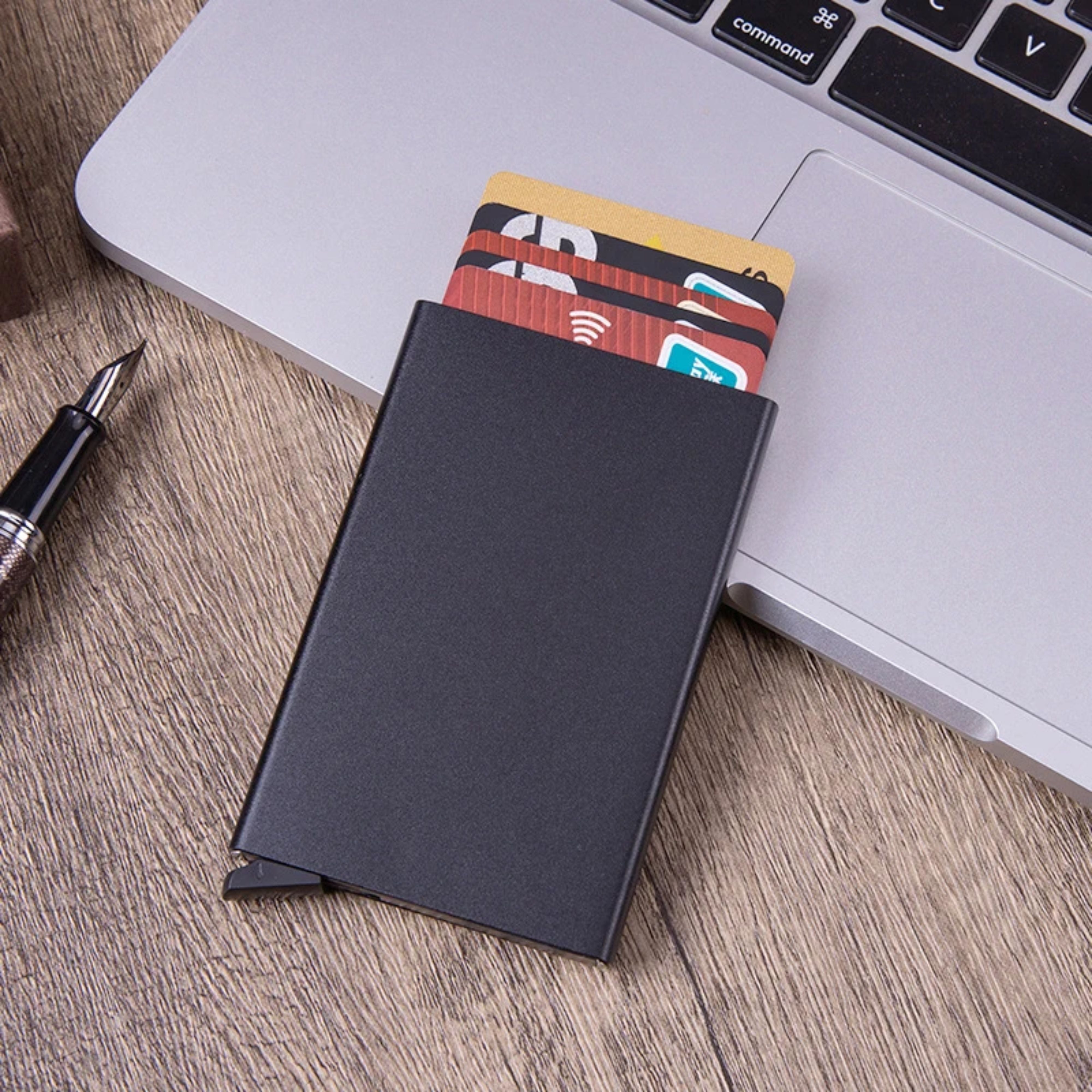 The stealth black ZeAiLi pop-up wallet placed neatly on a modern wooden office desk next to a pen and a laptop computer