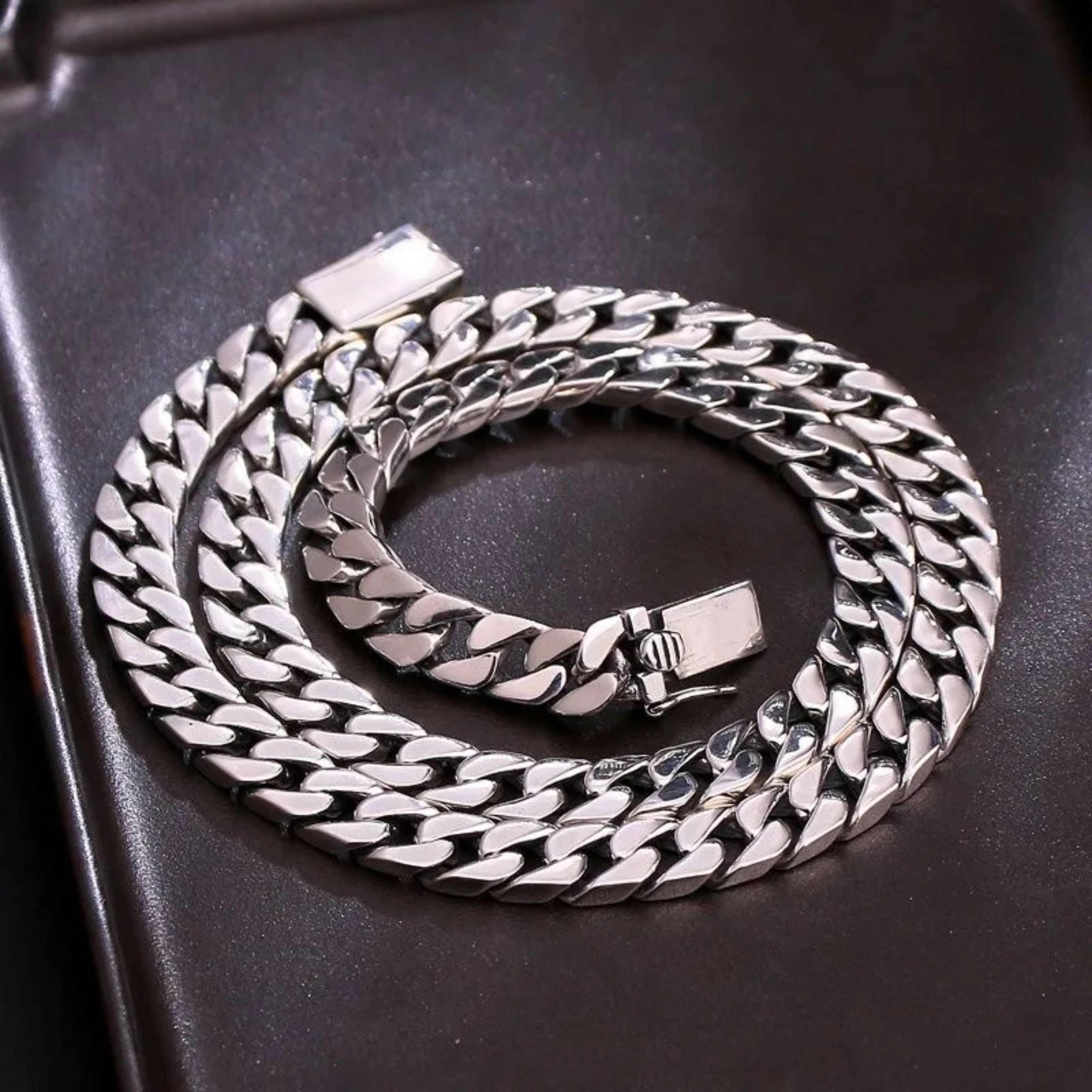 Polished silver Miami Cuban link chain perfectly coiled in a circle on a dark brown display tray.