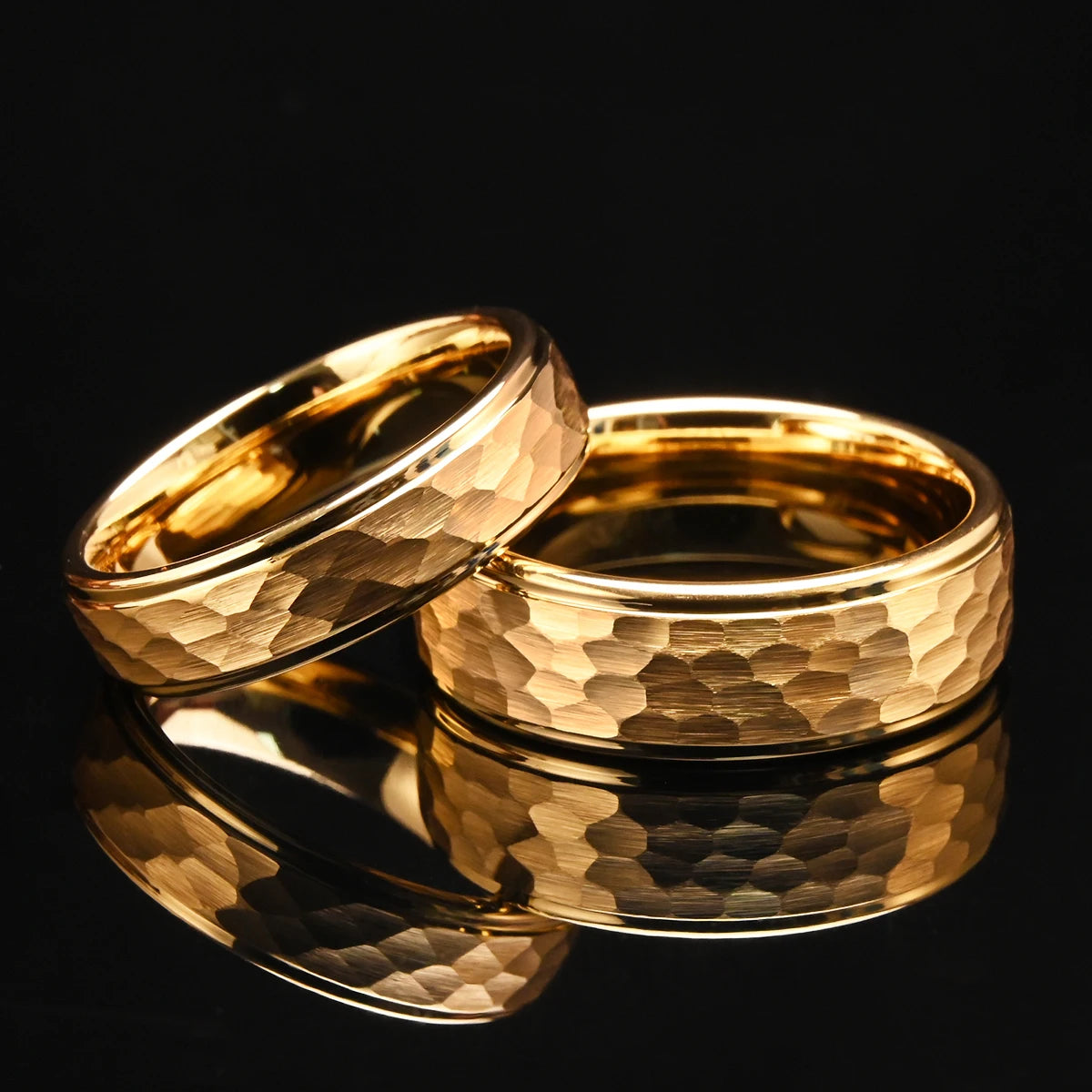 A pair of matching gold hammered tungsten carbide bands resting on a glossy black mirror, ideal for bridal and engagement sets