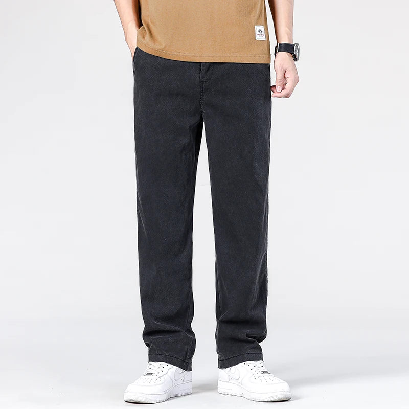 Front view of a model presenting the full-length dark charcoal black loose straight jeans styled with an orange tee and white sneakers