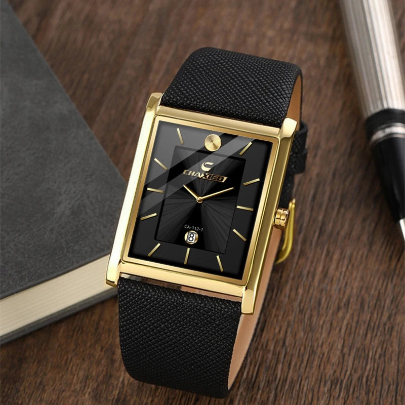 Gold rectangular men's dress watch with a black dial resting elegantly on a wooden desk next to notebooks and a pen.