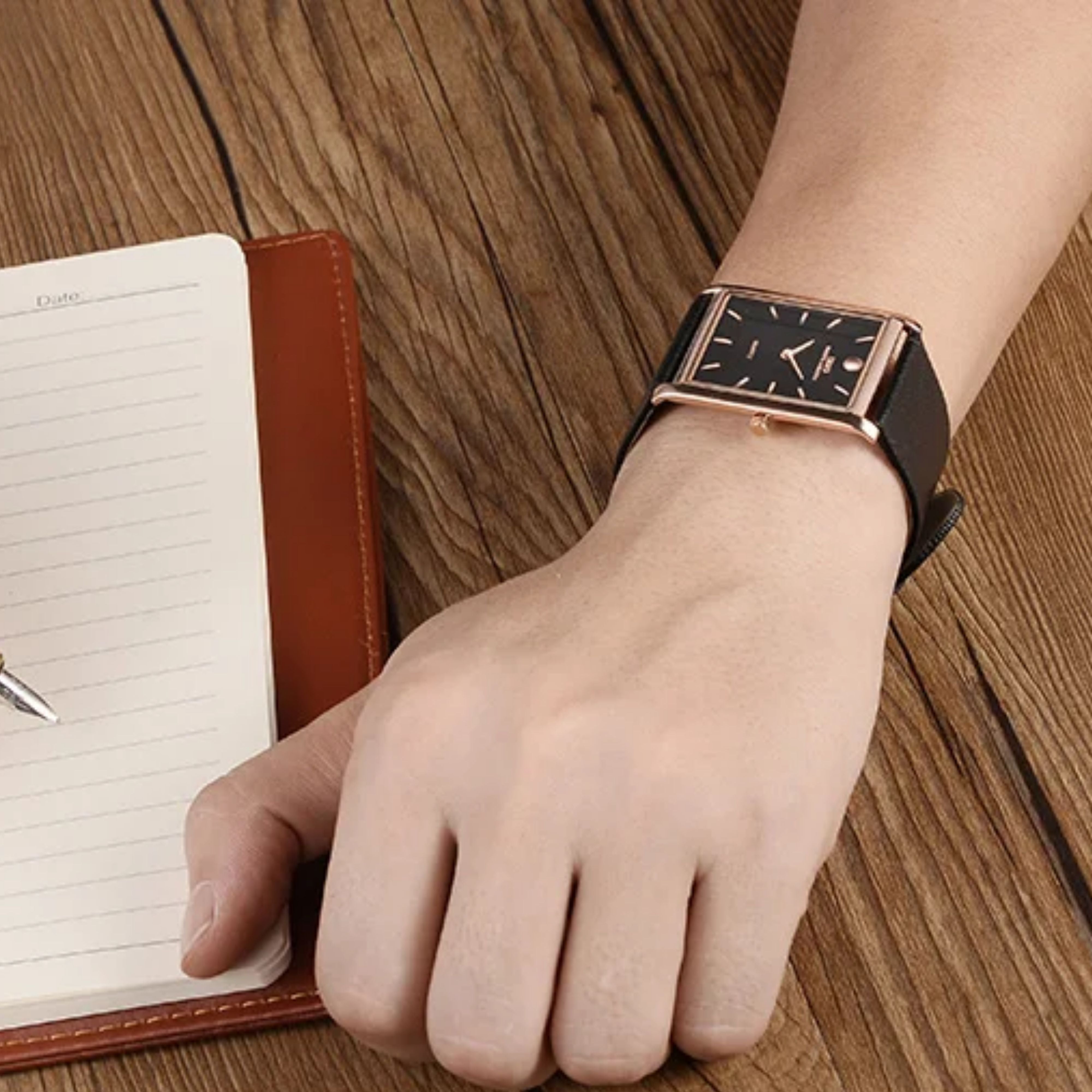A sharp close-up of the IBSO thin black-dial rectangular business watch being worn on a male model's wrist over a wooden tabletop background