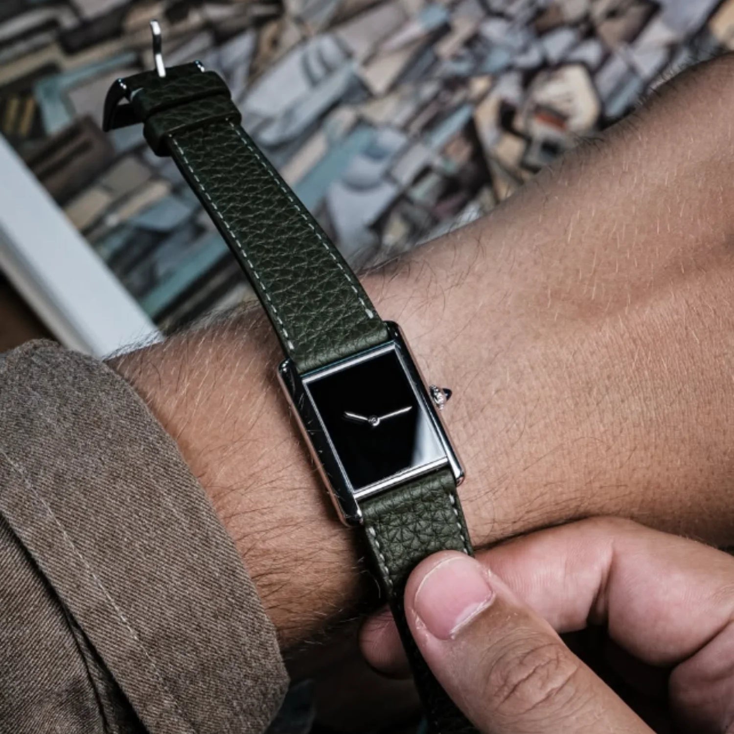A man adjusting his green leather strap CILOA square tank watch on his wrist, highlighting its vintage luxury casual appeal