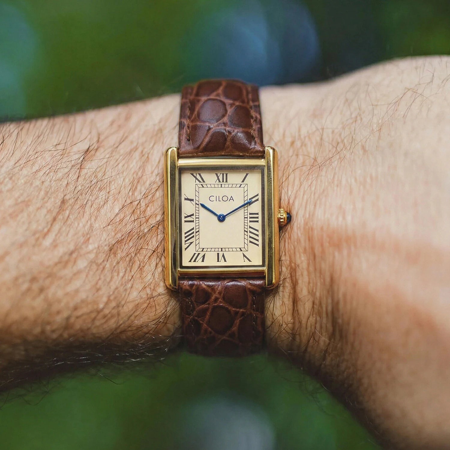 Close-up of the CILOA gold retro watch on a wrist under natural outdoor lighting, highlighting the cream Roman numeral dial and blue hands