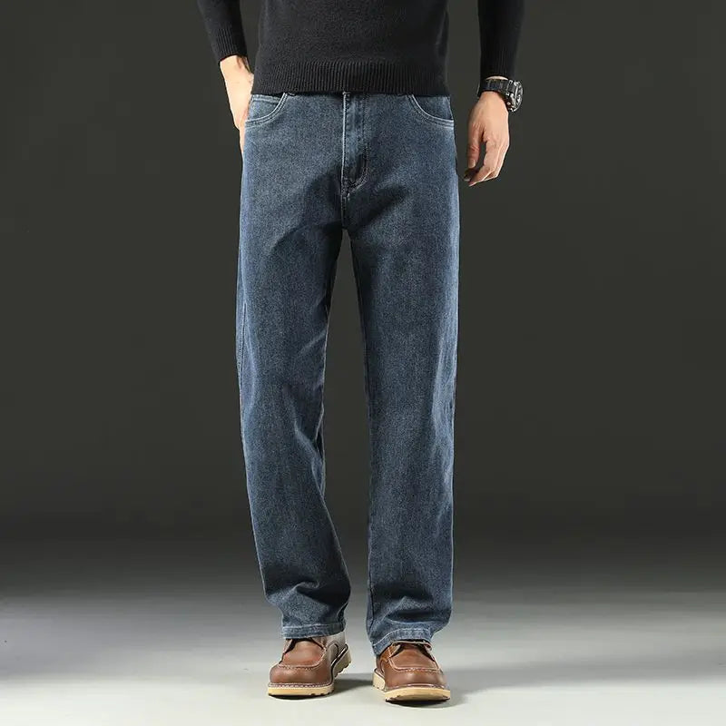 Front view of a male model wearing medium blue baggy straight stretch jeans paired with casual brown leather boots