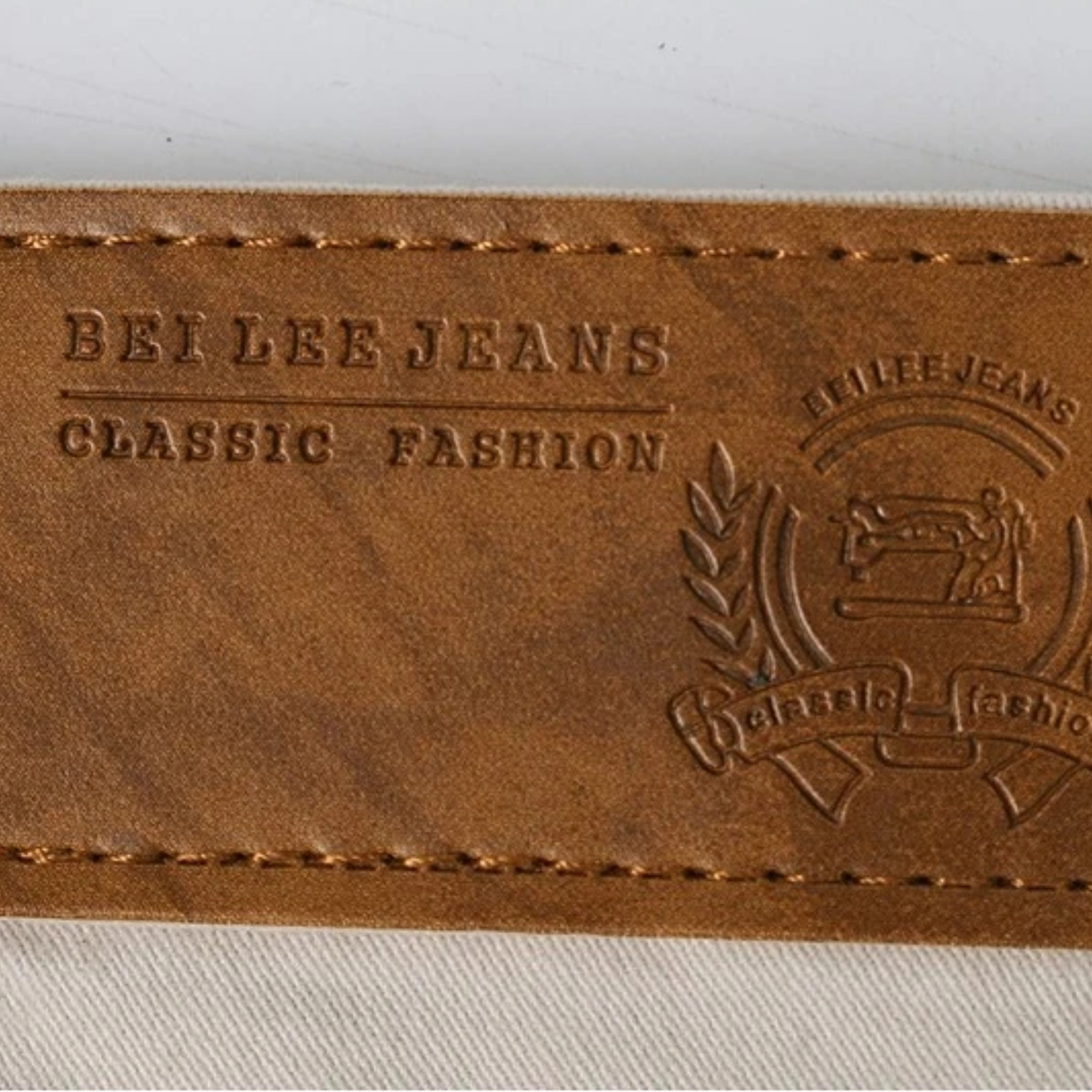 Macro close-up shot of the textured brown faux-leather waist label featuring embossed classic fashion denim branding text and crest graphics