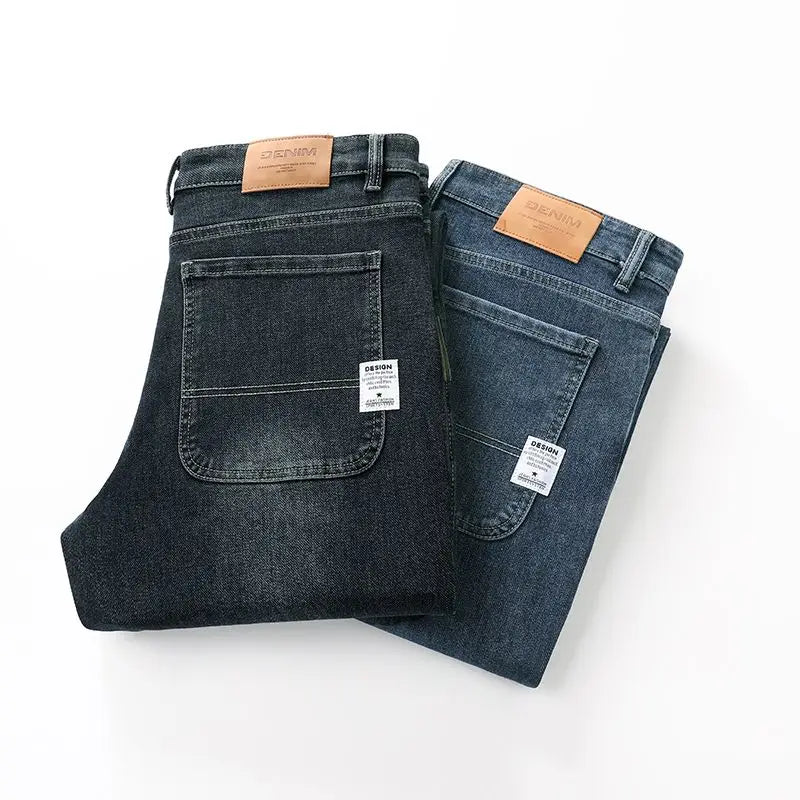 Two folded pairs of Tsingyi business denim pants in dark and medium blue, showcasing the back pockets with square white fabric tags and leather waist patches