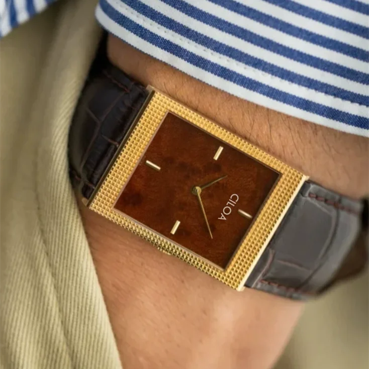 Model wearing a CILOA rectangular gold watch with a brown dial and leather strap, styled with a classic blue and white striped dress shirt.