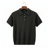 Front view of a dark olive green men's short-sleeve cable knit polo shirt with grey buttons hanging on a wooden hanger against a white background