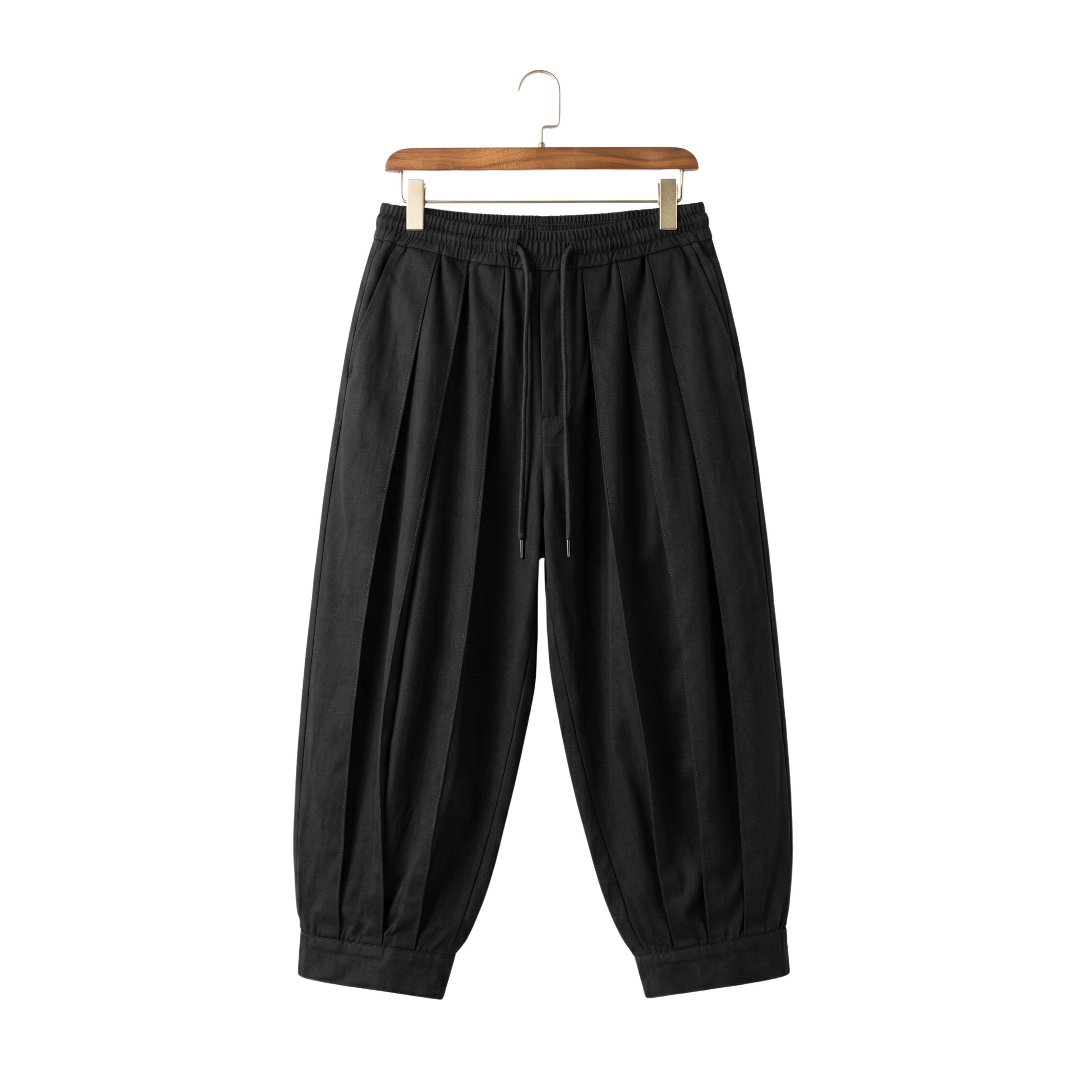 Front view of men's loose tapered harem pants in black with street fashion pleats on a wooden hanger