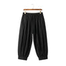 Front view of men's loose tapered harem pants in black with street fashion pleats on a wooden hanger