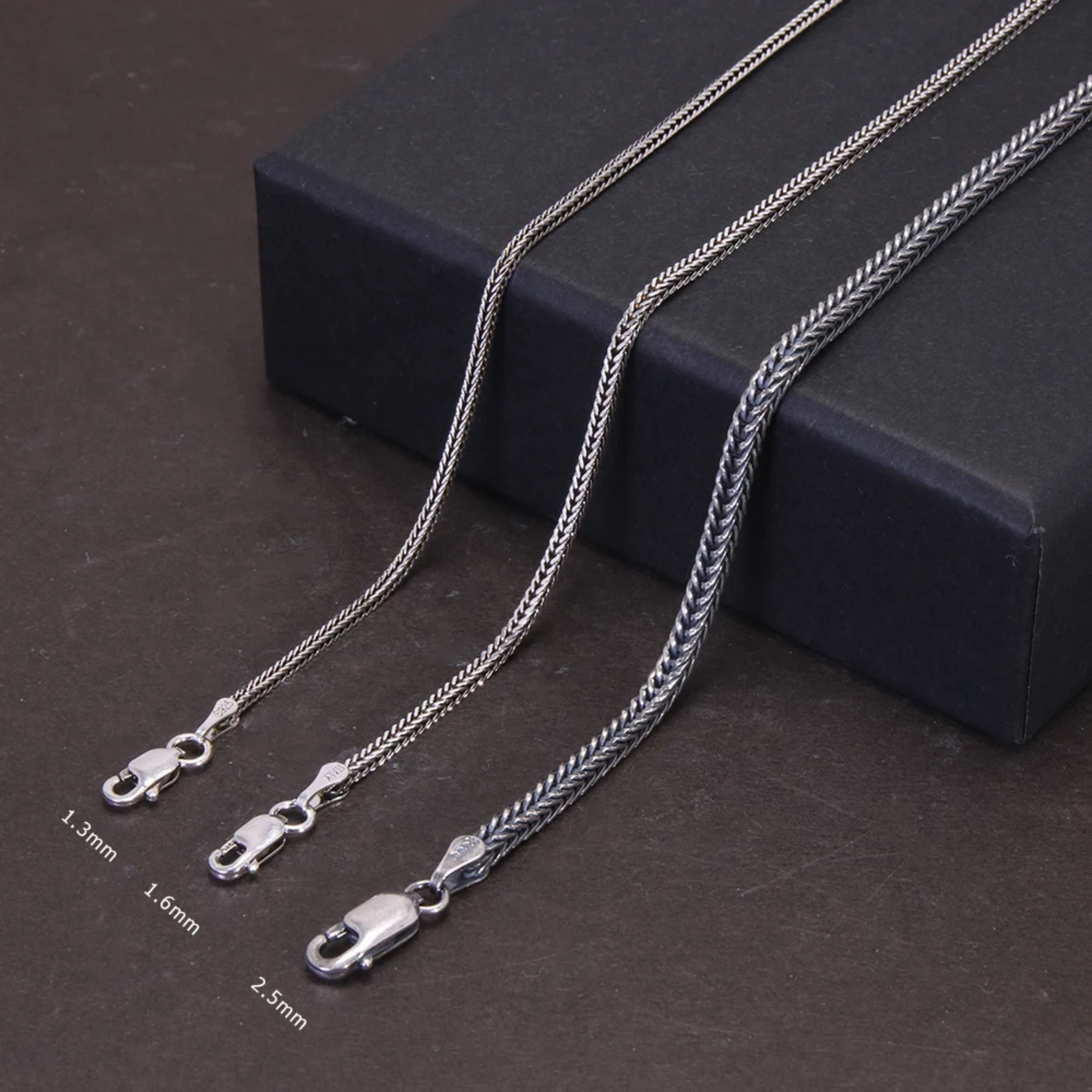 Three silver foxtail chain necklaces of varying lengths draped elegantly over a black display box.