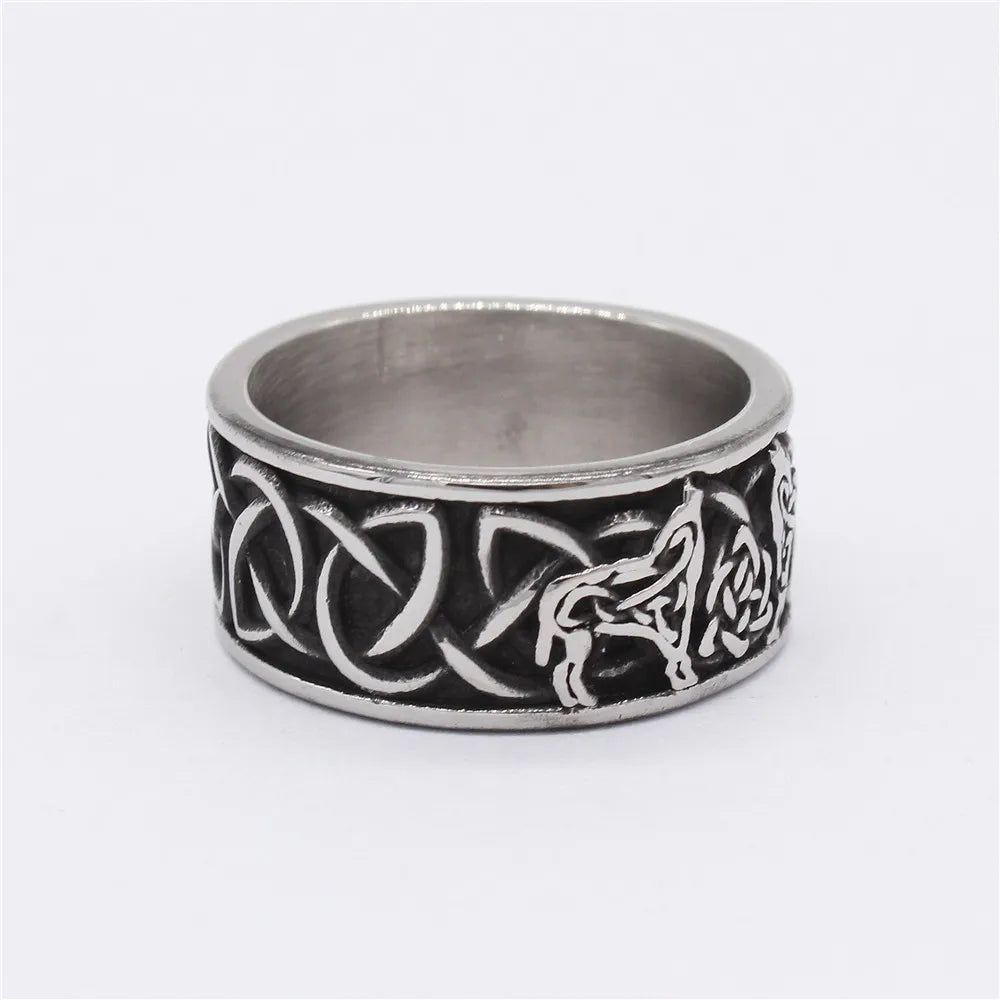 Oxidized silver band ring with a raised Celtic wolf and knot design standing upright on a light grey surface.
