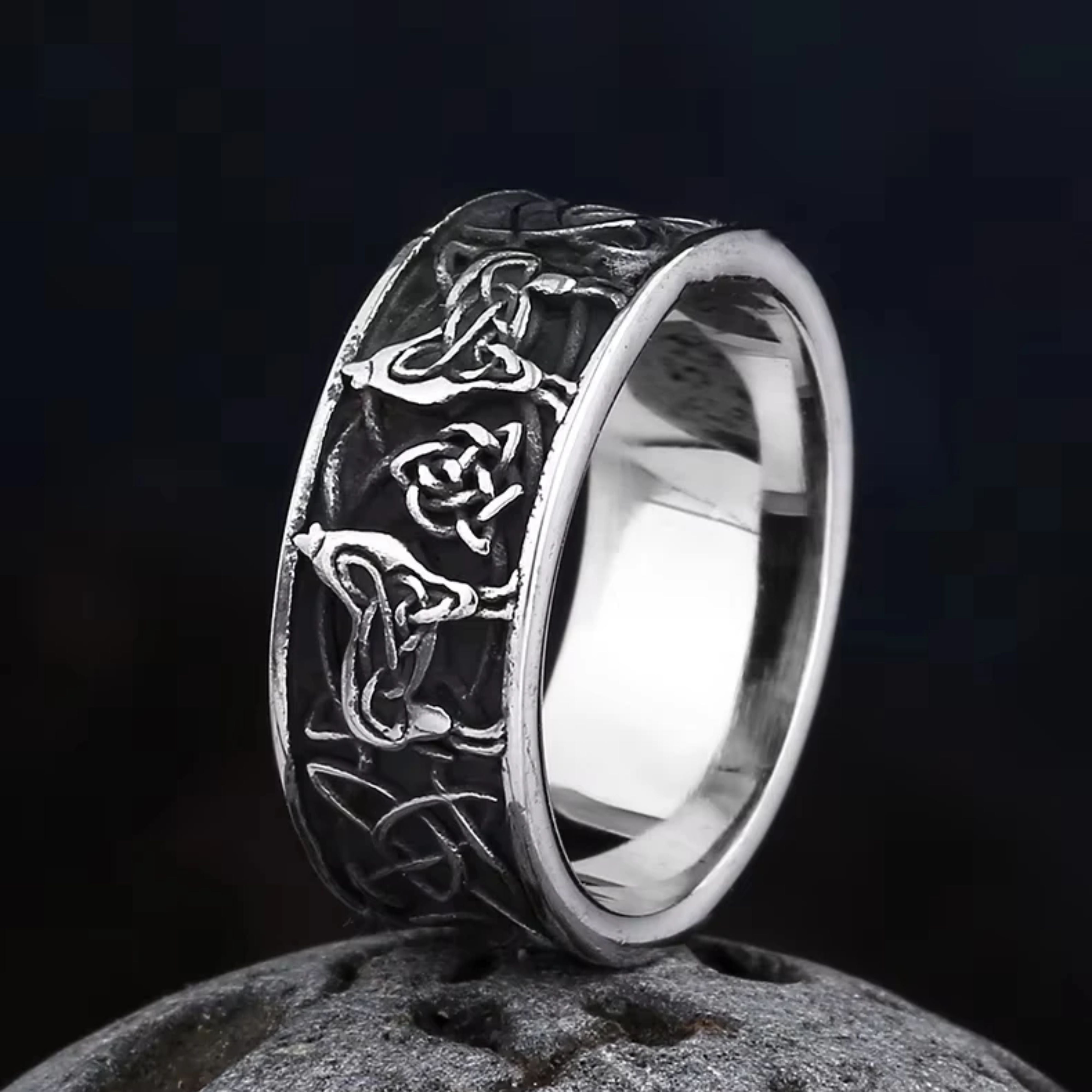 Angled view of an oxidized silver Viking wolf and knot ring resting on a dark stone, showing both the detailed exterior and smooth interior.