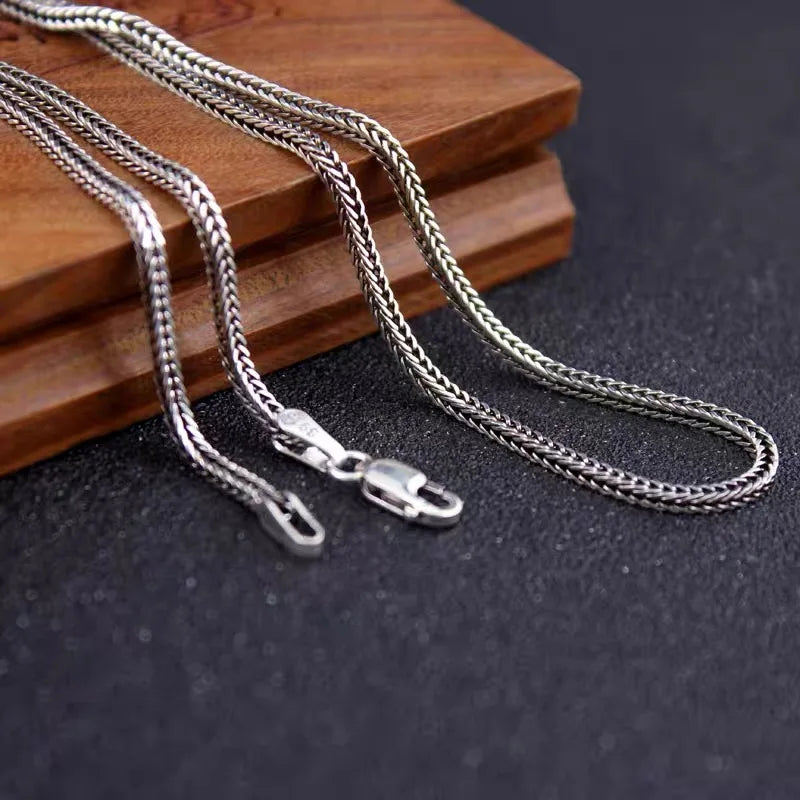 Oxidized silver wheat chain necklace draped on a dark slate surface next to a warm wooden block.