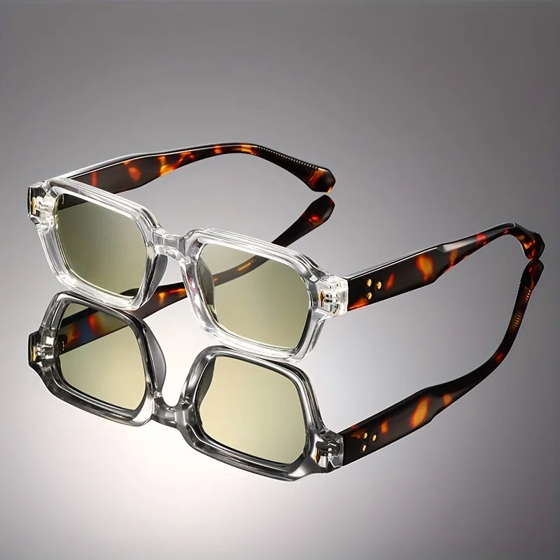 Retro chunky rectangular sunglasses with a clear front, tortoiseshell temples, and yellow lenses reflecting on a dark studio surface.