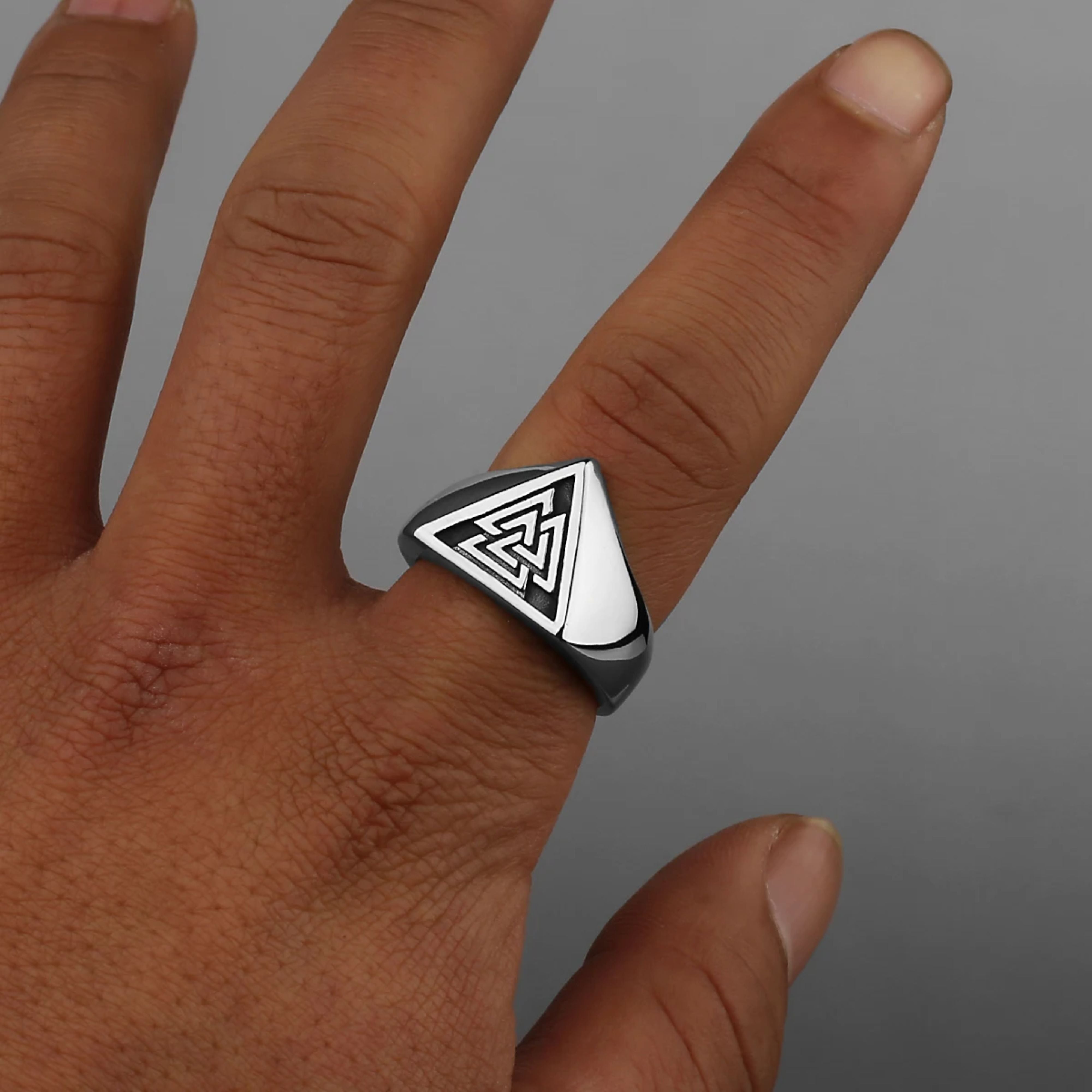 Retro silver ring engraved with the Valknut symbol displayed on a textured warm wooden block.
