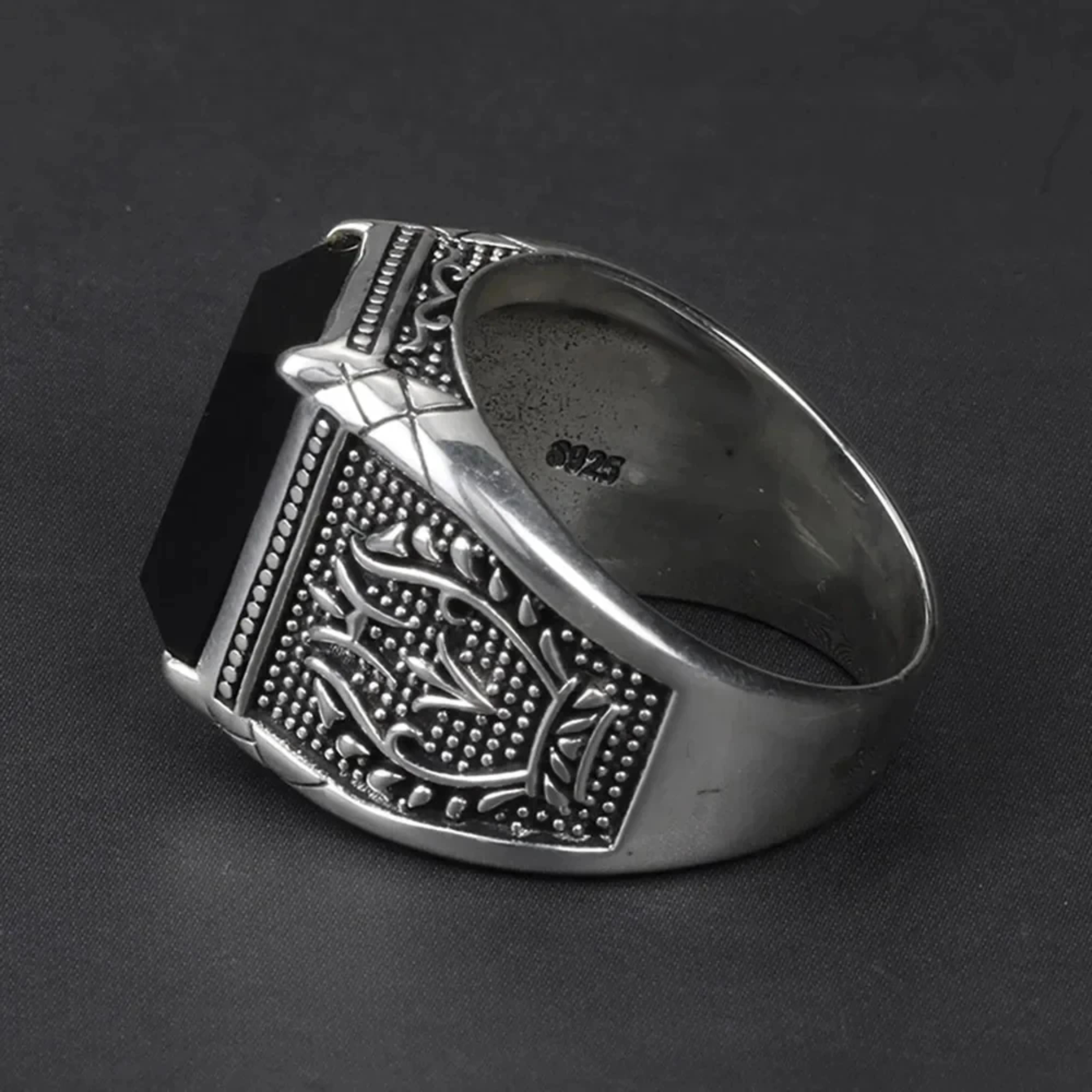 View of the smooth inner band and intricate side engraving of a men's silver black stone ring.