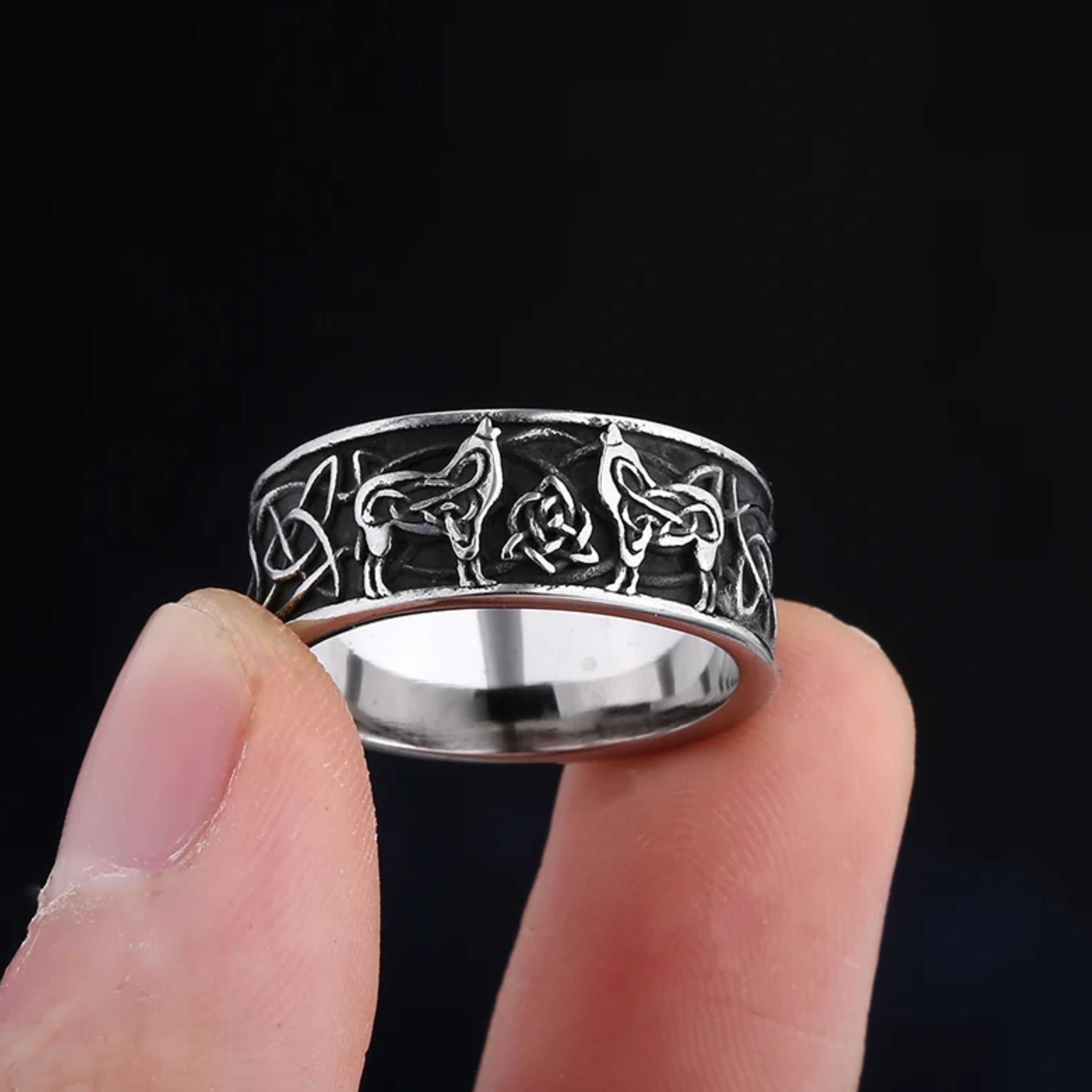 Close up of a silver Norse ring held between fingers, revealing two wolves facing a central Trinity knot.