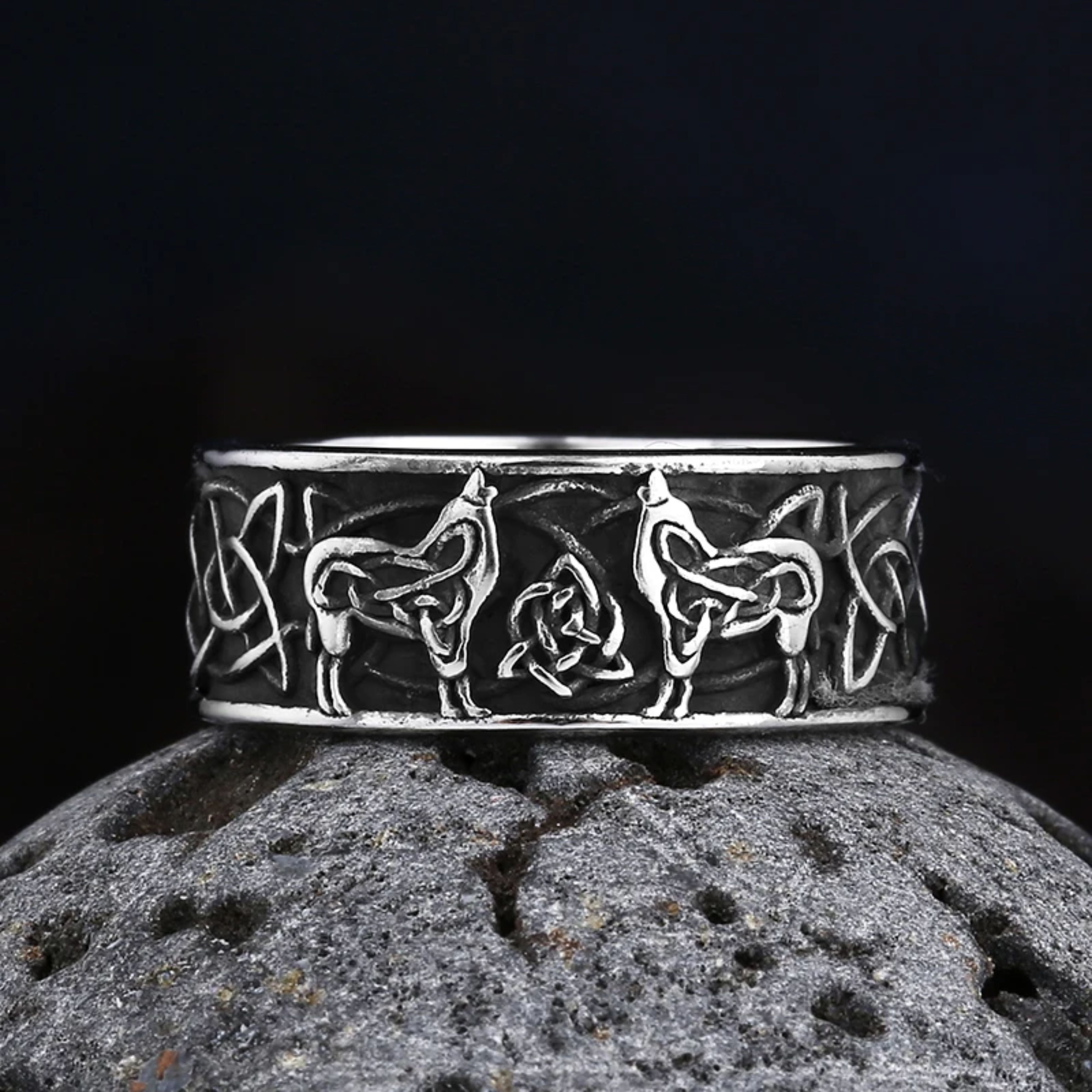 Silver Norse Fenrir wolf ring resting horizontally on a dark porous volcanic stone against a black background.