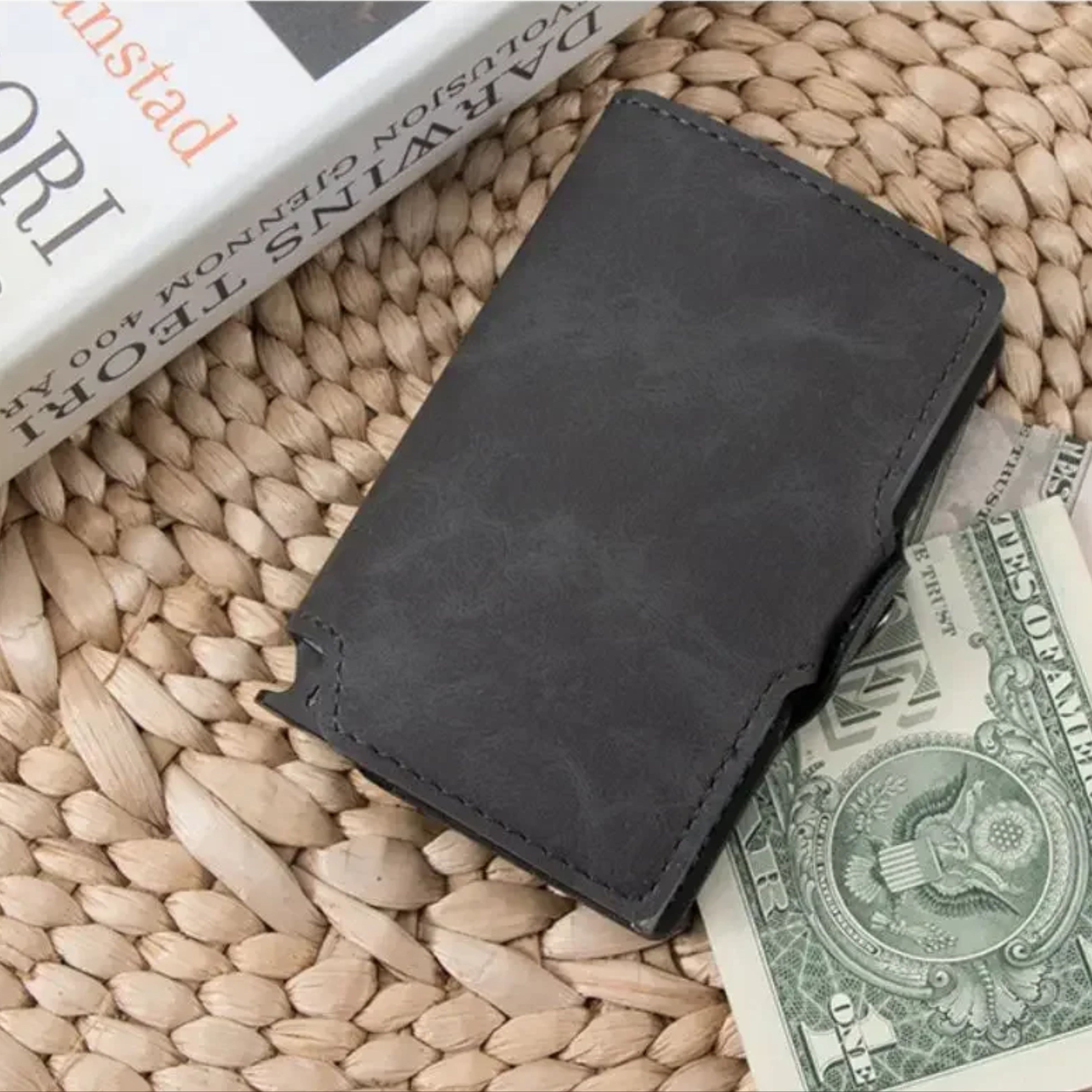 A rustic flat lay shot of the vintage black leather Smiley Sunshine mini wallet resting on a straw mat with a folded paper dollar bill peeking out