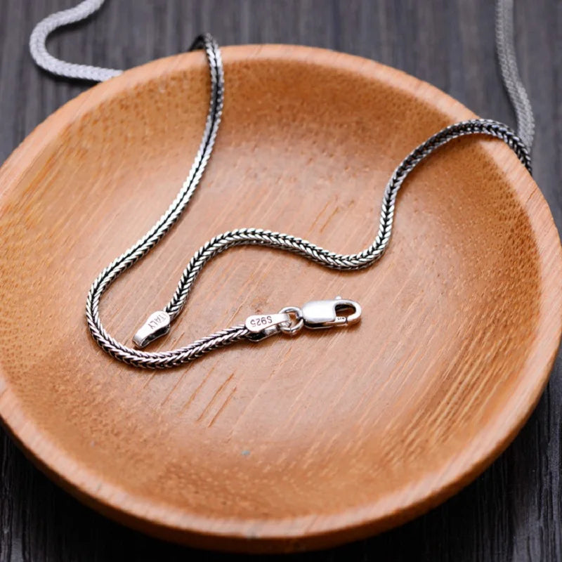 Vintage silver foxtail chain necklace resting loosely inside a round wooden display bowl.